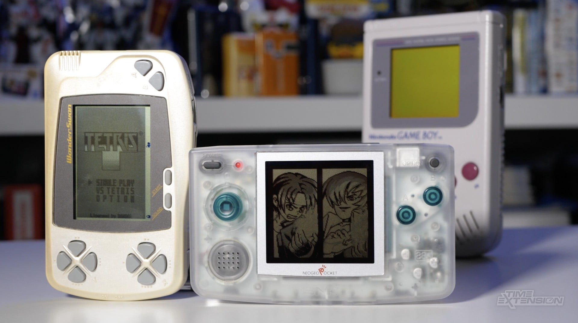 A retro handheld gaming setup with a Nintendo Game Boy style system and late 1990s portable consoles nearby